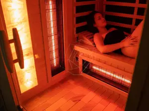 Inside a luxurious infrared home sauna with a Himalayan salt wall and subtle red light glow, showing a person experiencing deep relaxation and wellness benefits.